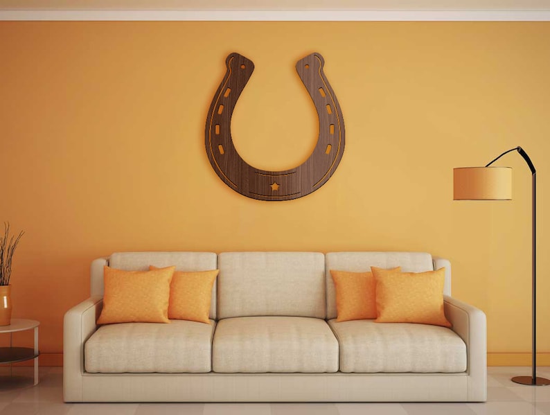 May include: A beige sofa with three orange throw pillows sits in front of a yellow wall with a large wooden horseshoe hanging on it. A floor lamp with a round lampshade is in the corner of the room.