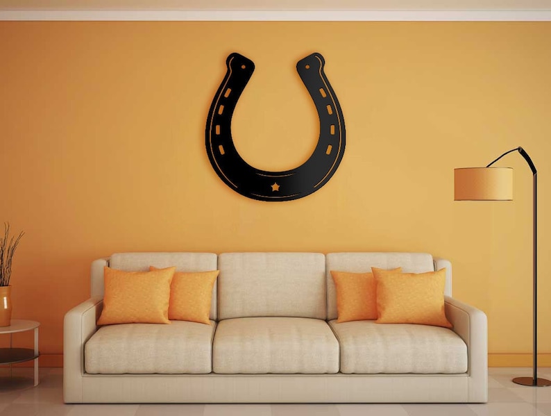 May include: A black metal horseshoe wall decor with a star in the center, hanging above a beige couch with orange throw pillows in a living room with a yellow wall and a floor lamp.