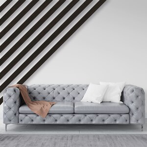 May include: A gray tufted sofa with two white pillows and a brown throw blanket. The sofa is in front of a white wall with black diagonal stripes.
