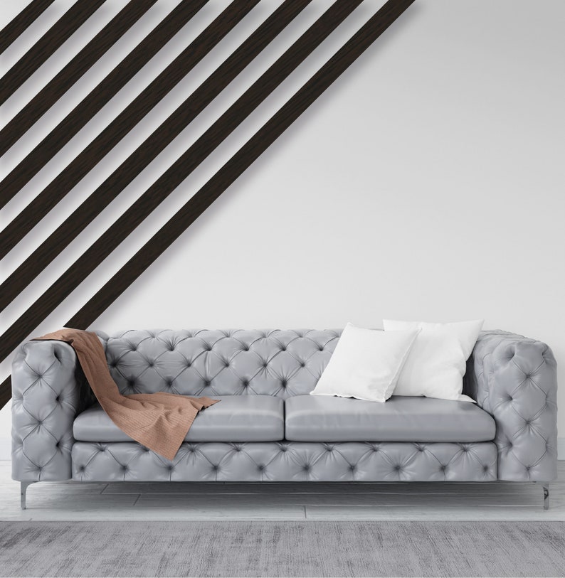 May include: A gray tufted sofa with two white pillows and a brown throw blanket. The sofa is in front of a white wall with black diagonal stripes.