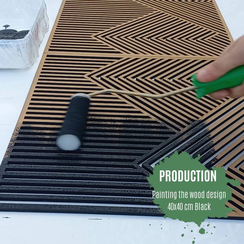 May include: A person is painting a wooden geometric design with black paint using a roller. The design is 40x40 cm and is called "Production: Painting the wood design 40x40 cm Black".