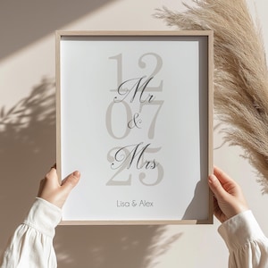 May include: A framed print with the text "Mr & Mrs" in a stylised font, with the numbers 12, 07, and 25 surrounding the text. The names Lisa & Alex are printed below the text.