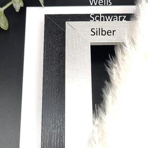 May include: Three picture frames in different colors: black, white, and silver. The frames are made of wood and have a textured finish. The text "Premium", "Wei&szlig;", "Schwarz", and "Silber" is visible on the frames.