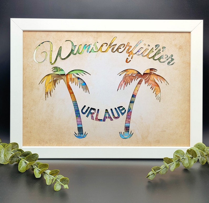 May include: A white framed picture with a brown background. The picture features two palm trees made of colorful paper, with the word "Wunschurlaub" above them and the word "Urlaub" between them.