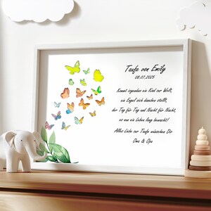 May include: A white framed print with a watercolor illustration of butterflies in various colors. The print includes the text "Taufe von Emily 08.07.2025" and a poem about a guardian angel watching over a child.