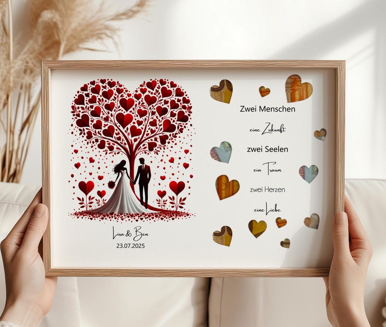 May include: A framed wedding art print featuring a tree with red heart-shaped leaves and a couple silhouette. The print includes the names "Lua & Ben" and the date "23.07.2025". Additional heart-shaped accents and text in German are also present.