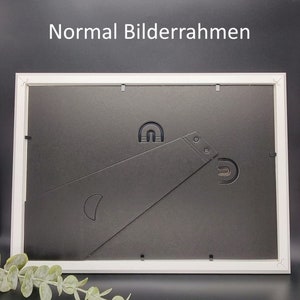 May include: The back of a white picture frame with a black backing. The frame has a built-in easel stand and a hanging hook.
