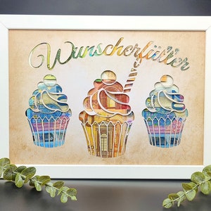 May include: A white frame with a brown background and the text "Wunschklitter" in gold lettering. Three cupcakes are cut out of the background and are made of euro bills.