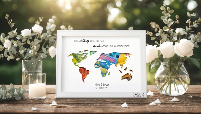 May include: A framed world map art print with a white frame. The map is filled with colorful patterns and text in German. The print is displayed on a wooden table with flowers and a candle.