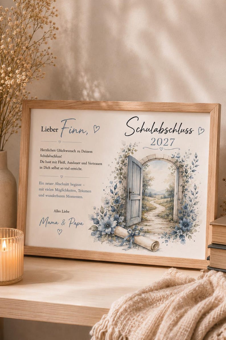 May include: A rectangular wooden frame containing a printed graduation message for Finn, dated 2027. The print features a stone archway with an open door, a winding path, blue floral accents, and a rolled diploma tied with a blue ribbon.