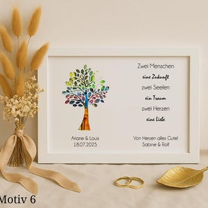 Könnte beinhalten: Ein weißer gerahmter Druck mit einem bunten Baumdesign und dem Text "Zwei Menschen, eine Zukunft, zwei Seelen, ein Traum, zwei Herzen, eine Liebe." Der Druck enthält auch den Text "Ariane & Louis 18.07.2025" und "Von Herzen alles Gute! Sabine & Rolf".