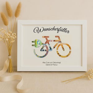 May include: White frame with a white mat and a black and white image of a bicycle made of money. The text "Wunschersch&uuml;ller" is at the top of the image. The text "Alles Gute zum Geburtstag Sabine & Marcus" is at the bottom of the image.
