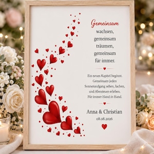May include: A framed print with a light wood frame features a romantic design. Red hearts cascade down the left side, with text in German. The text includes the names "Anna & Christian" and the date "08.08.2026".