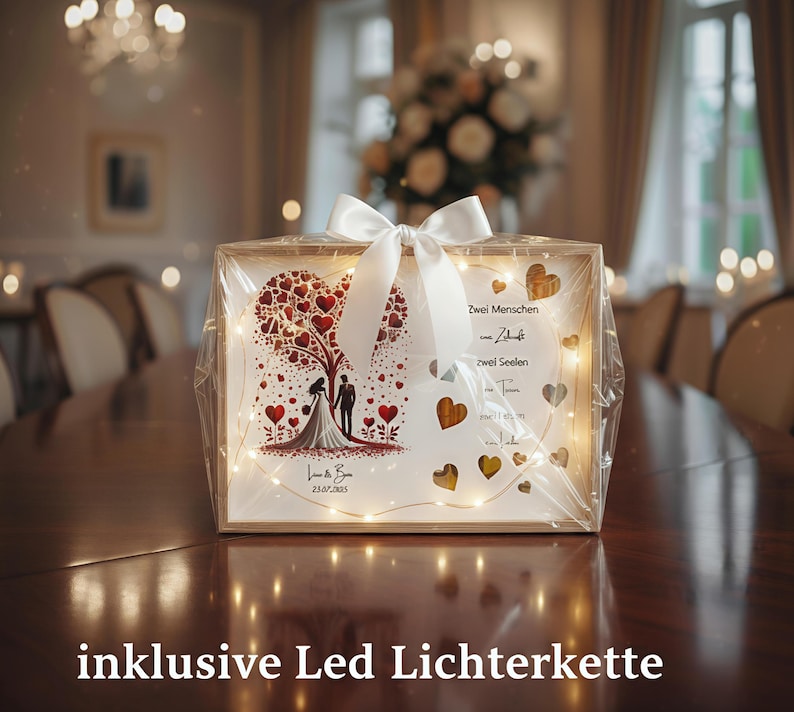 May include: A wooden framed wedding keepsake with a heart-shaped tree design, a bride and groom silhouette, and the date 23.07.2023. The frame is wrapped in clear cellophane and tied with a white ribbon. Includes LED string lights.