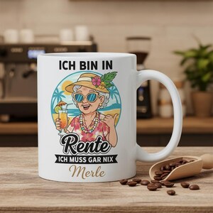 May include: White ceramic mug featuring a cartoon illustration of a woman in sunglasses and a straw hat, holding a tropical drink. The mug has text in German that reads "Ich bin in Rente, Ich muss gar nix, Merle."