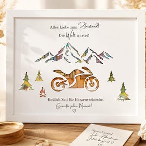 May include: A white framed print featuring a motorcycle silhouette filled with warm-toned patterns, set against a mountain range and pine trees. The text reads: Alles Liebe zum Ruhestand! Die Welt wartet! Endlich Zeit f&uuml;r Herzensw&uuml;nsche. Genie&szlig;e jeden Moment!