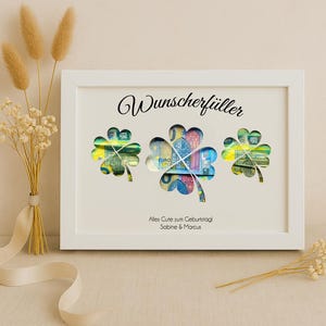 May include: White frame with a white background and the text "Wunschersch&uuml;ller" in black. Three shamrock-shaped cutouts are filled with euro banknotes. The text "Alles Gute zum Geburtstag Sabine & Marcus" is printed below the shamrocks.