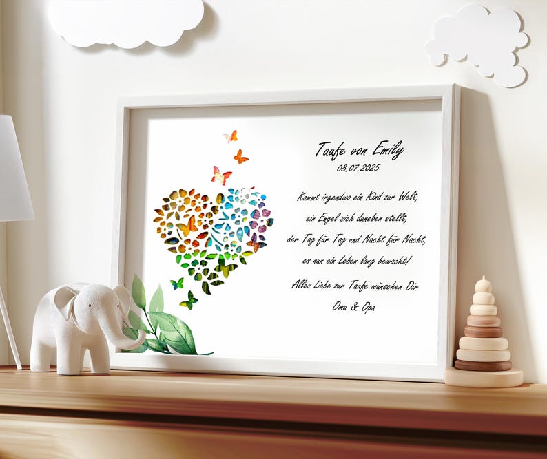 May include: A white framed print with a colorful heart made of butterflies and flowers. The text reads "Taufe von Emily 08.07.2025" and a poem about a child's baptism.
