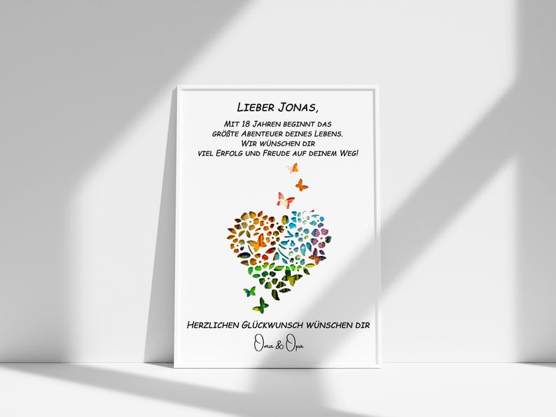May include: A white card with a black border and a message for a 18th birthday. The message reads "Lieber Jonas, Mit 18 Jahren beginnt das gr&ouml;&szlig;te Abenteuer deines Lebens. Wir w&uuml;nschen dir viel Erfolg und Freude auf deinem Weg!"  A colorful heart made of butterflies and flowers is in the center of the card. The card is signed "Oma & Opa".