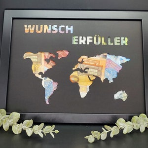 Puede incluir: Una imagen enmarcada en negro con un recorte de mapa del mundo. El mapa est&aacute; lleno de billetes de euro. Las palabras "Wunsch Erf&uuml;ller" est&aacute;n escritas en colores arco&iacute;ris en la parte superior del marco.