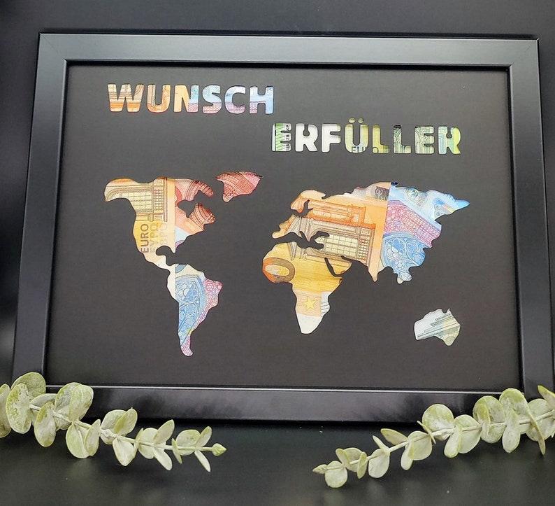 Puede incluir: Una imagen enmarcada en negro con un recorte de mapa del mundo. El mapa est&aacute; lleno de billetes de euro. Las palabras "Wunsch Erf&uuml;ller" est&aacute;n escritas en colores arco&iacute;ris en la parte superior del marco.