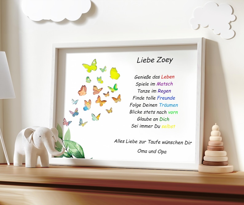 Puede incluir: Una impresi&oacute;n enmarcada con un dise&ntilde;o de mariposa de acuarela y un mensaje para una ni&ntilde;a llamada Zoey. El mensaje dice "Liebe Zoey" e incluye una lista de lecciones de vida, como "Genie&szlig;e das Leben" y "Sei immer Du selbst". La impresi&oacute;n es sobre fondo blanco y tiene un marco de madera claro. La impresi&oacute;n est&aacute; sobre un estante de madera con una figurita de elefante blanco y un juguete de apilar de madera.
