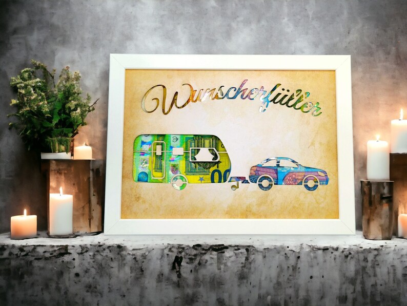 Puede incluir: Una imagen enmarcada en blanco con una caravana y un coche hechos de dinero en papel de colores. El texto "Wunsch erf&uuml;llt" est&aacute; escrito en letras doradas en la imagen.