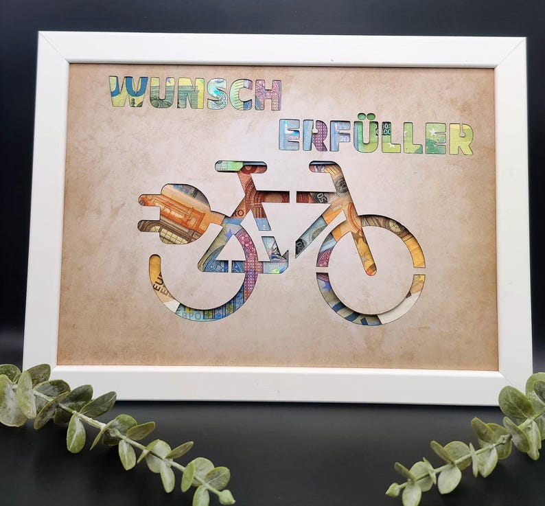 May include: A white rectangular frame containing a tan background with a cutout of a bicycle shape and the text WUNSCH ERF&Uuml;LLER. The cutout reveals colorful paper currency patterns behind the tan surface, creating a layered visual effect.