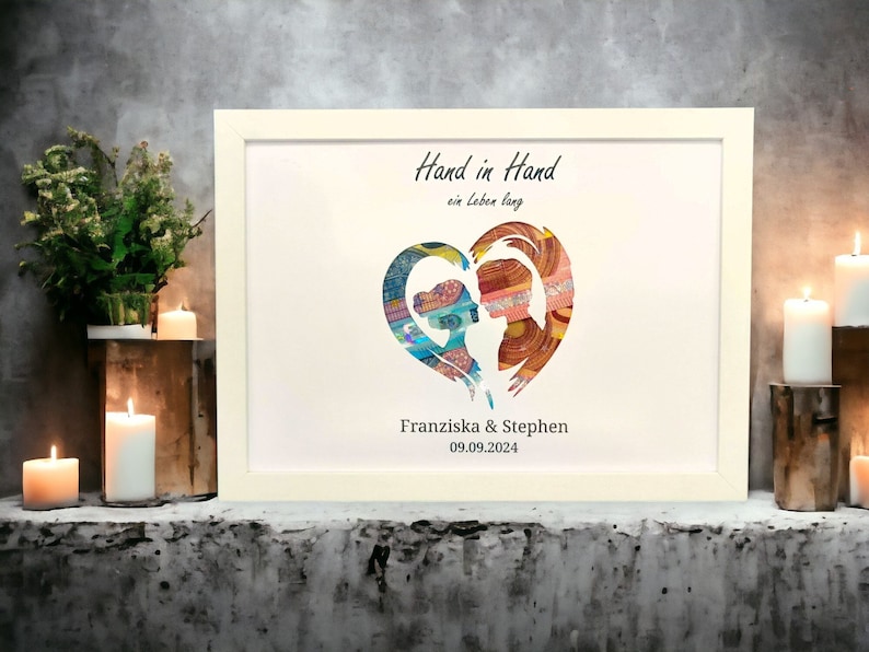 May include: Framed art print featuring two silhouetted figures within a heart shape, filled with colorful patterns. The text "Hand in Hand ein leben lang" is above the heart, with names and a date below. The frame is white.