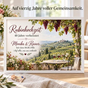 May include: A framed print featuring a vineyard landscape with a table, two wine glasses, and hanging grapes. The text reads: Auf vierzig Jahre voller Gemeinsamkeit. Rubinhochzeit 40 Jahre verheiratet Monika & Rainer Seit dem 08.08.1986 Auf alles, was uns verbindet.