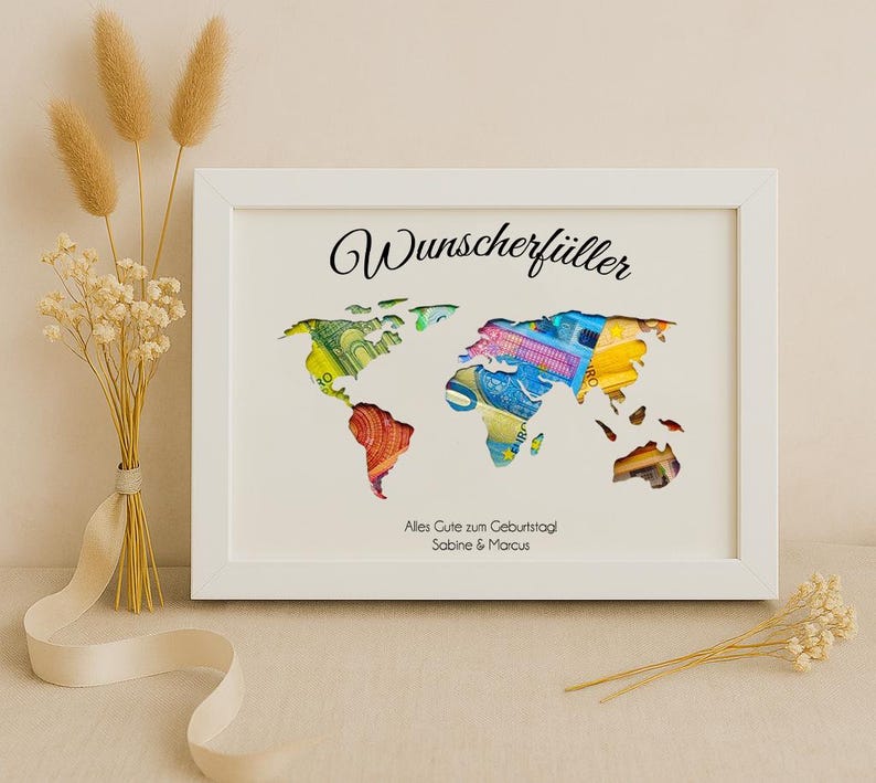 May include: White framed picture with a world map cutout filled with colorful paper money. The text "Wunschersch&uuml;ller" is at the top of the frame and "Alles Gute zum Geburtstag Sabine & Marcus" is at the bottom.