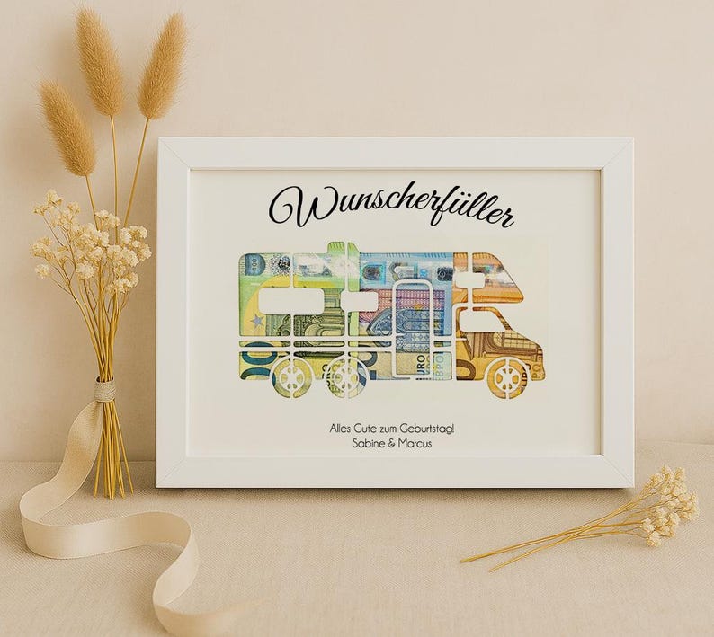 May include: A white frame with a white mat and a picture of a camper van made of euro bills. The text "Wunschersch&uuml;ller" is at the top of the frame. The text "Alles Gute zum Geburtstag Sabine & Marcus" is at the bottom of the frame.