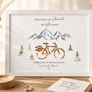 May include: A white framed print featuring a mountain range, a bicycle, and pine trees with a plaid pattern. The text reads: Alles Liebe zum Ruhestand! Die Welt wartet! Endlich Zeit f&uuml;r Herzensw&uuml;nsche. Genie&szlig;e jeden Moment! A small card below reads: Neues Kapitel. Dein Abenteuer. Jetzt beginnt's!