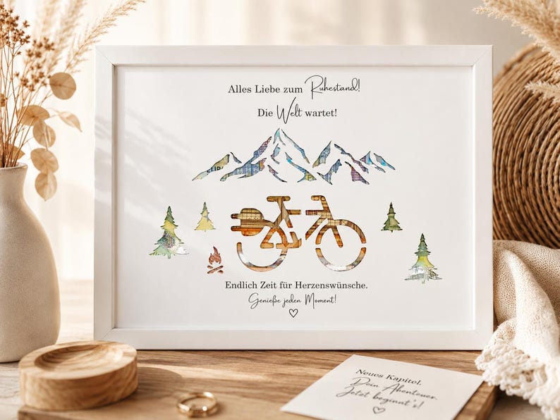 May include: A white framed print featuring a mountain range, a bicycle, and pine trees with a plaid pattern. The text reads: Alles Liebe zum Ruhestand! Die Welt wartet! Endlich Zeit f&uuml;r Herzensw&uuml;nsche. Genie&szlig;e jeden Moment! A small card below reads: Neues Kapitel. Dein Abenteuer. Jetzt beginnt's!