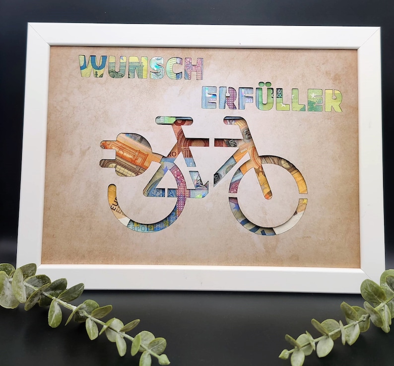 Puede incluir: Un marco blanco con un fondo marr&oacute;n. Las palabras "Wunsch Erf&uuml;ller" est&aacute;n recortadas del fondo y reemplazadas por dinero en papel de colores. Una silueta de bicicleta est&aacute; recortada del fondo y reemplazada por dinero en papel de colores.