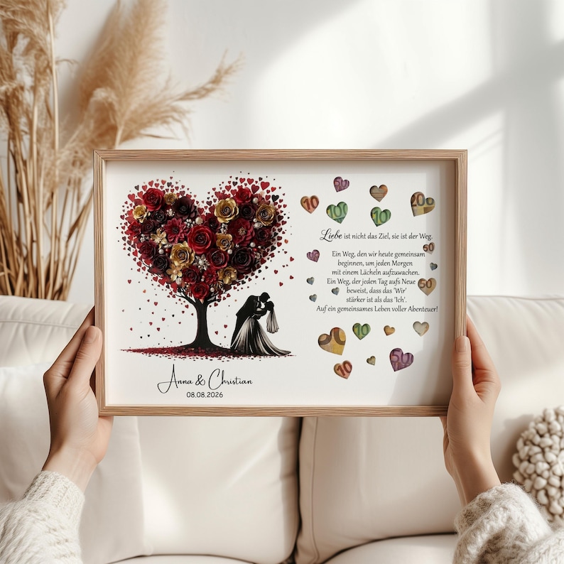 May include: A framed print featuring a heart-shaped tree composed of red and gold roses. Below the tree, a silhouette of a couple embraces. The print includes text in German and the names "Anna & Christian" with the date "08.08.2026".