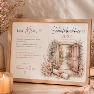 May include: A rectangular wooden frame containing a personalized graduation print for Mia, dated 2027. The print features German text, a watercolor illustration of an open door leading to a path, pink flowers, and a rolled diploma tied with a ribbon.