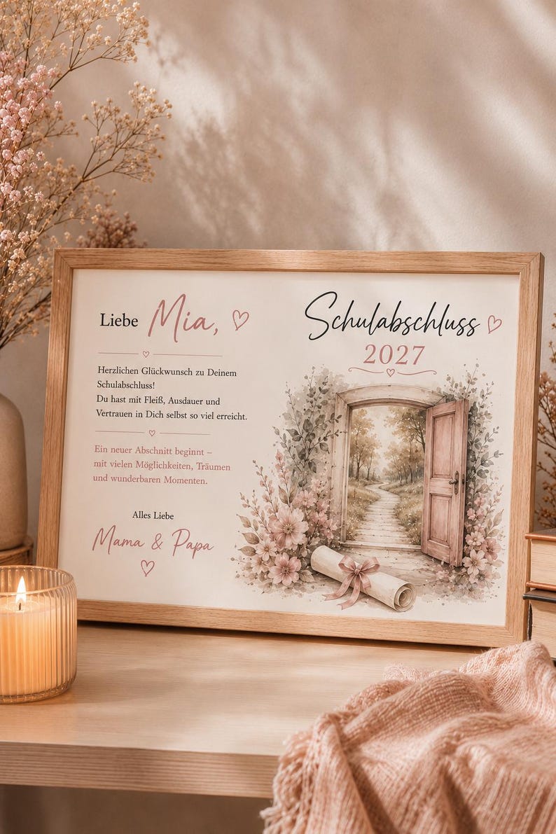 May include: A rectangular wooden frame containing a personalized graduation print for Mia, dated 2027. The print features German text, a watercolor illustration of an open door leading to a path, pink flowers, and a rolled diploma tied with a ribbon.