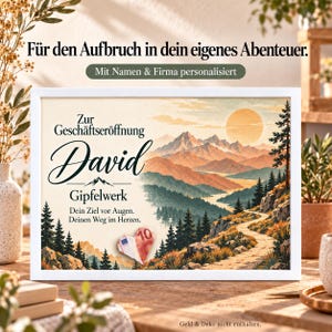 Può includere: Una cornice bianca contenente una stampa di un paesaggio montano con sole, un sentiero e pini. Il testo recita: Für den Aufbruch in dein eigenes Abenteuer. Mit Namen & Firma personalisiert. Zur Geschäftseröffnung David Gipfelwerk. Dein Ziel vor Augen. Deinen Weg im Herzen. Una banconota da 10 euro piegata a forma di cuore è fissata sulla stampa.