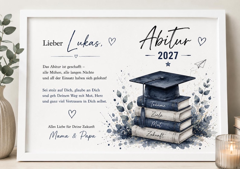 Pu&ograve; includere: Una stampa bianca incorniciata con il testo 'Lieber Lukas, Abitur 2027' e un messaggio di congratulazioni in tedesco. Il design include un'illustrazione ad acquerello di un tocco di laurea appoggiato su quattro libri etichettati Tr&auml;ume, Ziele, Mut, Zukunft.