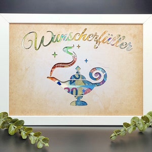 May include: A white frame with a tan background and a cutout of a genie lamp made from money. The text "Wunsch erf&uuml;llt" is written in a decorative font above the lamp.