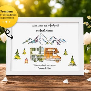 May include: A framed watercolor print with a white border, featuring a camper, mountains, and trees. The text reads "Alles Liebe zur Hochzeit! Die Welt wartet!" and "W&uuml;nschen Euch von Herzen". The image is decorated with flowers and a lit candle.