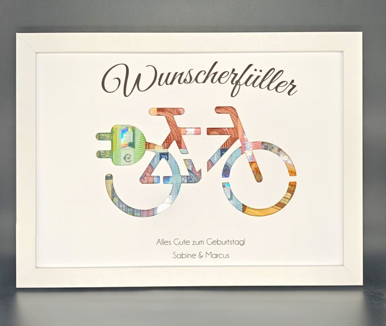 K&ouml;nnte beinhalten: Ein wei&szlig; gerahmtes Bild mit wei&szlig;em Hintergrund. Das Bild zeigt ein Fahrrad aus Geld mit einem Stecker vorne. Der Text "Wunscherf&uuml;ller" befindet sich oben im Bild. Der Text "Alles Gute zum Geburtstag Sabine & Marcus" befindet sich unten im Bild.