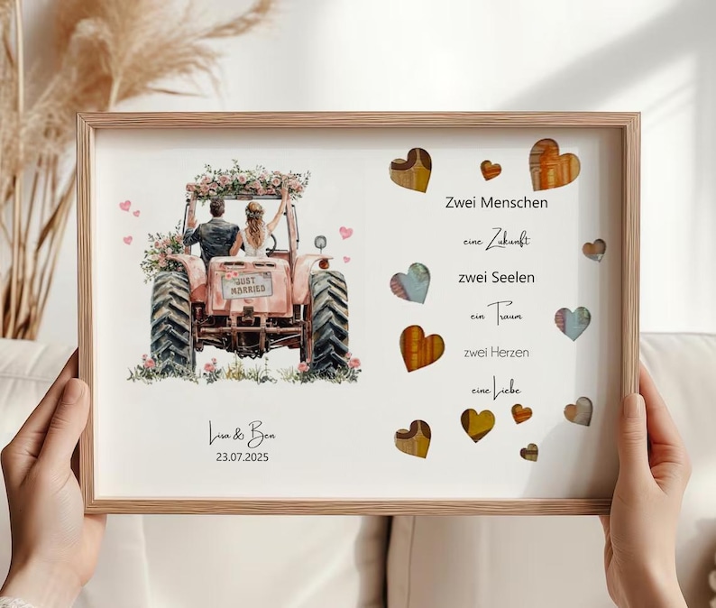 May include: A framed print featuring a watercolor illustration of a couple on a pink tractor, with floral accents. The text "Just Married" is visible on the tractor. The print also includes the names "Lisa & Ben" and the date "23.07.2025". Decorative hearts are scattered around the text.