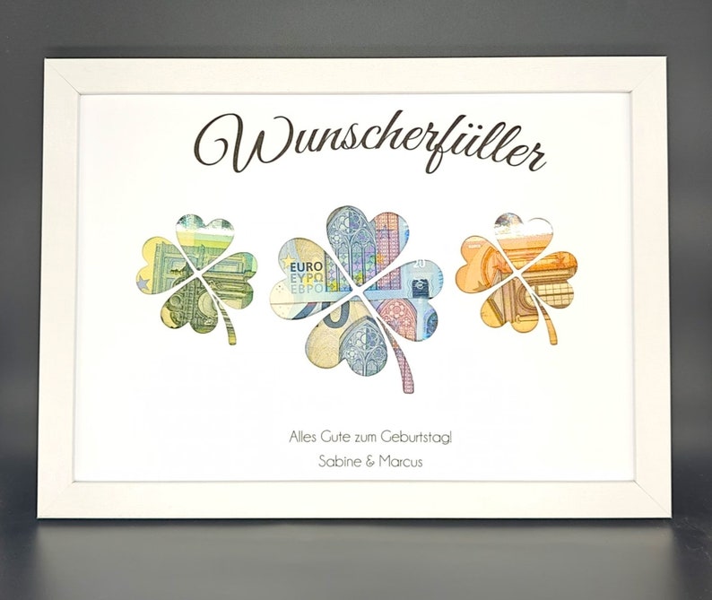 K&ouml;nnte beinhalten: Ein wei&szlig;er Rahmen mit wei&szlig;em Hintergrund und dem Text "Wunschersf&uuml;ller" in schwarzer Schrift. Drei vierbl&auml;ttrige Kleebl&auml;tter sind aus dem Hintergrund ausgeschnitten und mit Euro-Banknoten gef&uuml;llt. Der Text "Alles Gute zum Geburtstag! Sabine & Marcus" ist unter den Kleebl&auml;ttern gedruckt.