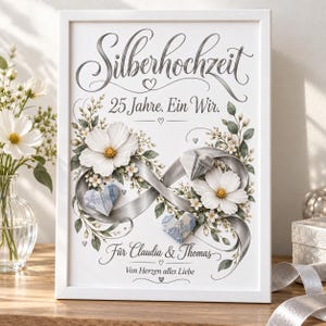 May include: A white framed print featuring the text Silberhochzeit, 25 Jahre. Ein Wir., Für Claudia & Thomas, and Von Herzen alles Liebe. The design includes a silver infinity ribbon, white flowers, green leaves, and three folded paper hearts.