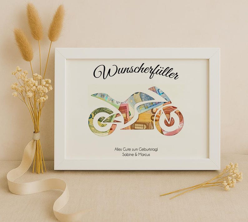 May include: A white frame with a white mat and a motorcycle silhouette made of money inside. The text "Wunschersch&uuml;ller" is at the top of the frame. The text "Alles Gute zum Geburtstag Sabine & Marcus" is at the bottom of the frame.