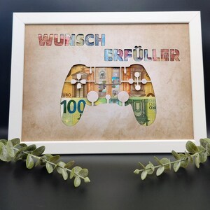May include: A white rectangular frame containing a tan mat with the cutout text WUNSCH ERF&Uuml;LLER and a game controller shape. Behind the cutouts, Euro banknotes are visible, showing various colors and the number 100 on a green bill.