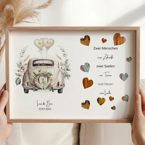 Può includere: Una stampa incorniciata con un'illustrazione di un'auto d'epoca, decorazioni floreali e palloncini. La stampa include i nomi "Lisa & Ben" e la data "23.07.2025". Sono presenti anche cuori di legno decorativi e testo in tedesco.
