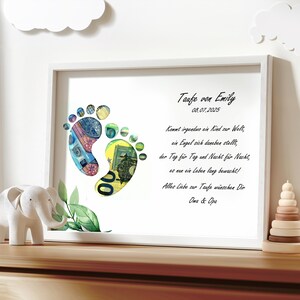May include: A white framed print with a poem about a baby's arrival. The poem is written in German. The print features two baby footprints made of money. The footprints are surrounded by green leaves. The print is titled "Taufe von Emily" and the date "08.07.2025" is printed below the title.